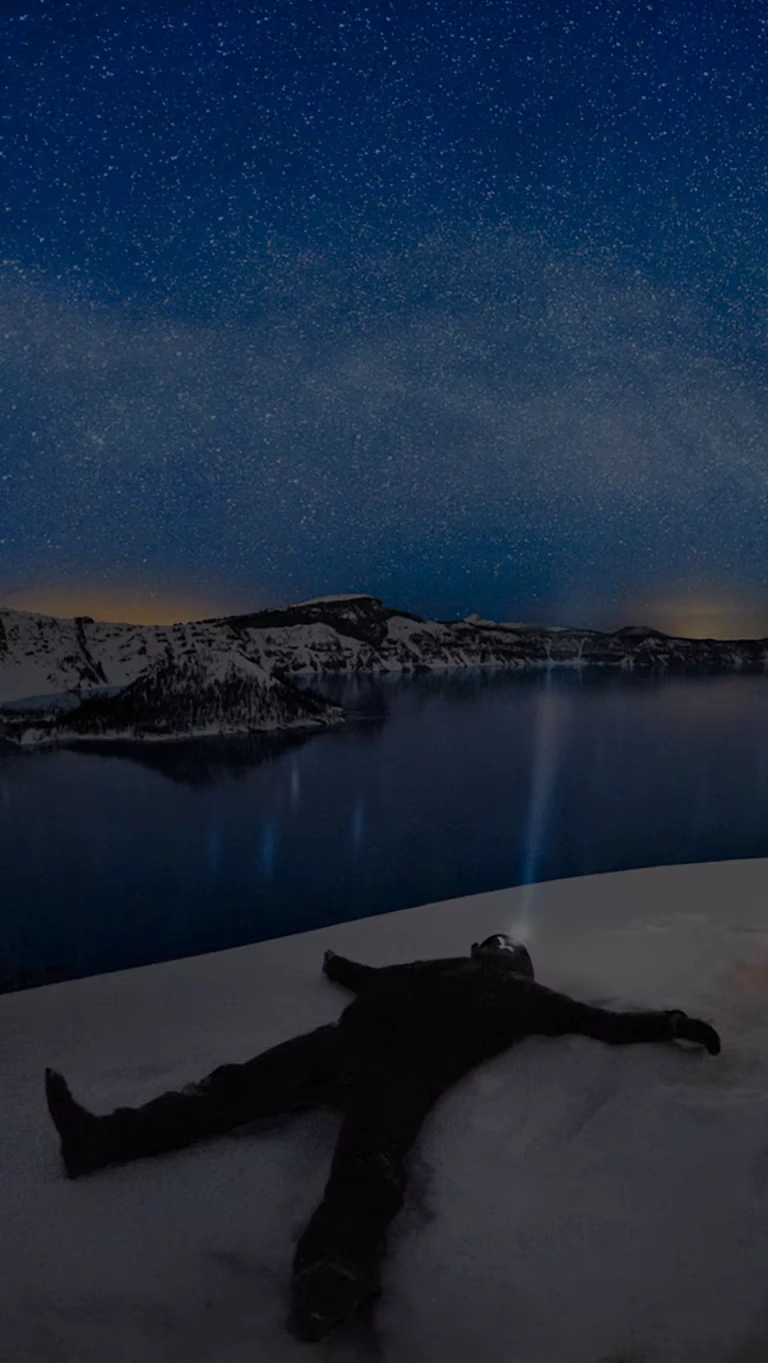 A winter camper gazes at a clear night sky while overlooking Crater Lake.